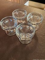 Four clear glass sherbet dessert bowls arranged on a surface, showing top and side views.
