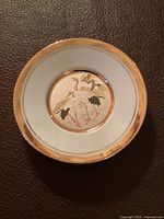 Top-down view of round plate with white and gold rim featuring two cranes and pine branch design in the center.