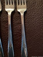 Close-up photo showing the handle design and prongs of two silver-plated forks with floral pattern.