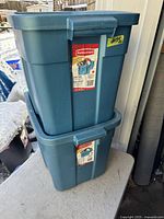 Photo showing two stacked blue Rubbermaid Roughneck totes with front labels and attached lids. Small crack visible on one tote.