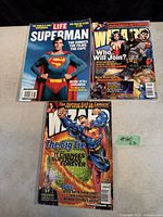 Three Superman magazines displayed flat, showing covers: LIFE Superman with actor, Empire magazine with Superman Returns, and Superman comic styled cover titled 'The Big Lie'.