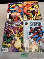 Photo showing four Superman comic books with colorful covers featuring Superman, Flash, Wonder Woman, and other characters.
