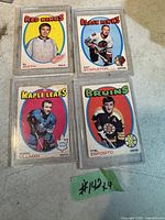Four vintage 1969-70 hockey cards featuring Al Smith (Red Wings), Pat Stapleton (Black Hawks), Norm Ullman (Maple Leafs with chip), and Phil Esposito (Bruins) placed on surface with green lot number tag.