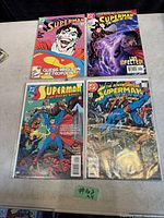Four vintage Superman comic books displayed on a surface, each in a protective sleeve showing different cover art and titles.