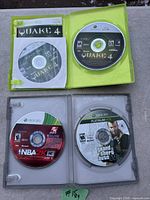 Four Xbox 360 Game discs: Quake 4 with case and manual, NBA 2K13 disc in empty case, Grand Theft Auto V Platinum Hits with case.