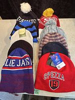 View of 10 assorted toques in various colors and styles, some with sports logos and pom-poms, neatly arranged on a tabletop.