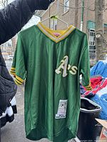 Green Oakland Athletics baseball jersey front view showing 'A's' logo on chest, collar, sleeve details and sewn patch on front bottom left.