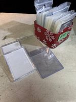 Photo showing multiple packs of clear plastic card sleeves in a holiday-themed container, with loose sleeves laid flat to show size and clarity.