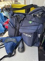 Multiple CCM Goliath hockey pants with visible padding and straps, plus McKenney groin guard and protective insert on table.