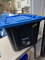 Black Mastercraft heavy-duty storage tote with blue lid shown from side angle.