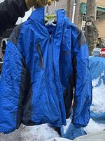 Front view of blue and black men's winter coat with hoodie and zipper pocket on chest.