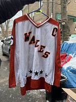 Front view of white and orange NHL Wales jersey with #66 on sleeve, 'WALES' arched across chest, captain 'C' on upper front right, on hanger outside