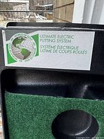 Close-up of the label on the black tray showing 'Ultimate Electric Putting System' and the brand 'World of Golf' in green and white.