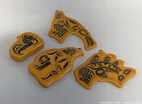 Four vintage handmade Haida pendants with black tribal designs on yellow base arranged on a table, showing variation in shapes and sizes.