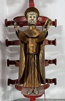 Front view of red iron frame with gilded saint figurine and hanging bells