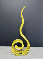 Yellow and blue swirled art glass sculpture on a dark surface and background, showing twisted, spiral shape and smooth finish.