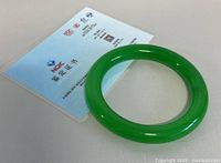 Bangle positioned diagonally on white textured surface next to certification card