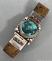 Close up top view of Navajo silver leather bracelet showing large round turquoise stone and small turquoise and coral inlays on silver.