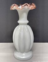 Front view of vintage Fenton milk glass vase with ribbed bulbous body and pink ruffled top edge.