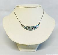 Front view of abalone crescent pendant on thin silver-tone chain displayed on jewelry stand.