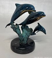 Front view of vintage dolphin sculpture showing three dolphins leaping from stylized wave base.