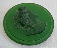 Photo of vintage green glass cabochon cameo showing profile of woman with flowers in hair, from a slight angle highlighting details and minor wear.