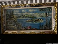 Front view of the framed 3D landscape artwork showing a lake with island, mountains, trees, and garden plants inside decorative gold and beige frame.