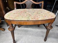 Photo of a wooden bench with floral fabric seat upholstery showing detailed front view of seat and legs.
