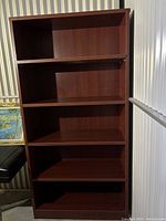 Full front view of the wooden bookcase showing five evenly spaced shelves and vibrant brown finish.