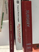 Spine view of five books showing titles: Old Gardens, Reproductive Health Care Manual, Diet for a Small Planet 20th Anniversary Edition, Surgery by Lange 1973.