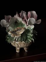 Front view of ceramic vase with pink and green sculpted flowers and leaves, showing details of petals and leaves, standing on four legs.