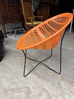Side view of the orange chair showing molded plastic seat with slotted pattern and black metal legs.