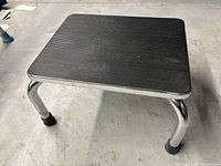 Black platform foot stool with ribbed surface and chrome metal legs.