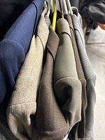 Photo showing six men's blazers on hangers in various colors including blue, beige, olive, gray with stripes, and brown.