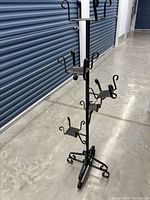 Photo of black metal plant stand with multiple holders and a sturdy base on a concrete floor by blue storage unit doors.