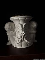 White ceramic vase with two cherubs as handles and wing details between them, with green floral sponge in the opening.