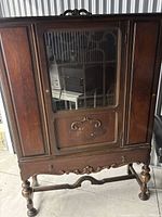 Front view of the wooden cabinet showing glass door with decorative wooden trimmings and carved bottom panel.