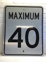 Front-facing photo of the rectangular reflective road sign showing the full text 'MAXIMUM 40' with slight scratches and mounting holes.
