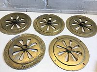 Five painted gold circular adjustable vent covers placed side by side on a white surface. Each vent cover has a flower petal pattern cutout and an adjustable center mechanism.