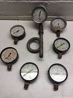 Overview photo showing seven small gauges including one with an attached metal pipe loop.