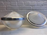 Both banded acorn holophane globes displayed side by side on surface against brick wall, showing overall size and shape.