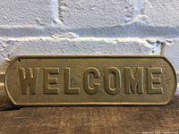 Front view of brass welcome sign showing full embossed lettering and textured background.