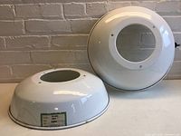 Two white enamel dome light shades resting on a surface, showing the overall shape and size.