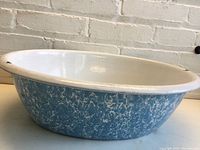 Side angle photo of the blue and white speckled enamelware basin outside against a brick wall, showing its oval shape and size.