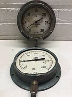 Front view of two round pressure gauges, one showing 0-300 PSI scale, the other 0-30 PSI, both with Morrison Brass branding, showing wear and some rust