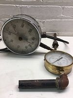 Two vintage pressure gauges with metal and brass casings showing signs of wear, rust, and tarnish with visible pressure measurement dials.