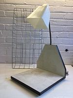 Desk lamp with plastic shade positioned in front of wire file tray against brick wall background.