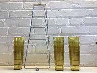 12 yellow pebble plastic tumblers stacked in two groups of six next to metal wire magazine holder against white brick background