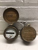Two Neptune gas meters as a lot, showing the iconic brass hinged covers and vintage dial face for measuring gallons of liquid, marked 'IN' inside the cover.