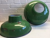 Pair of green enamel lamp shades with dark blue edges, showing rust and wear spots on the surface, photographed from front angle.